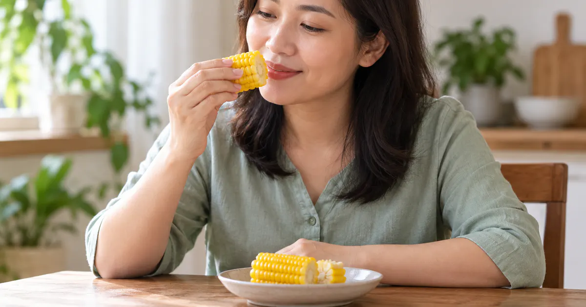 trào ngược dạ dày ăn ngô được không: người phụ nữ ăn ngô luộc mềm tại bàn